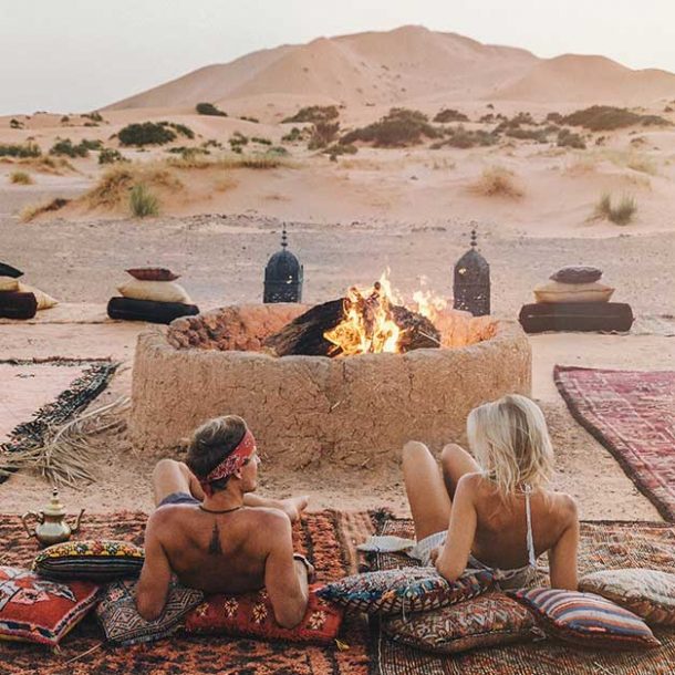 Two influencers looking the Sahara desert of Merzouga in Morocco around the firepit in a camp.